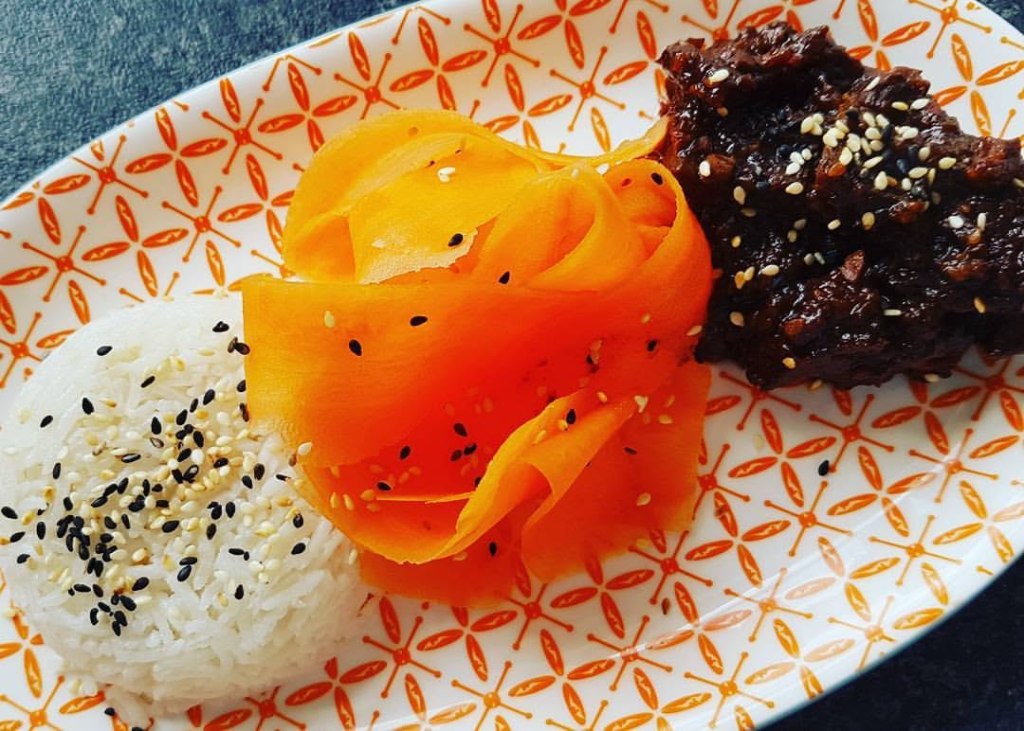 Mongolian-style beef served with rice, carrot ribbons and mixed black and white sesame seeds