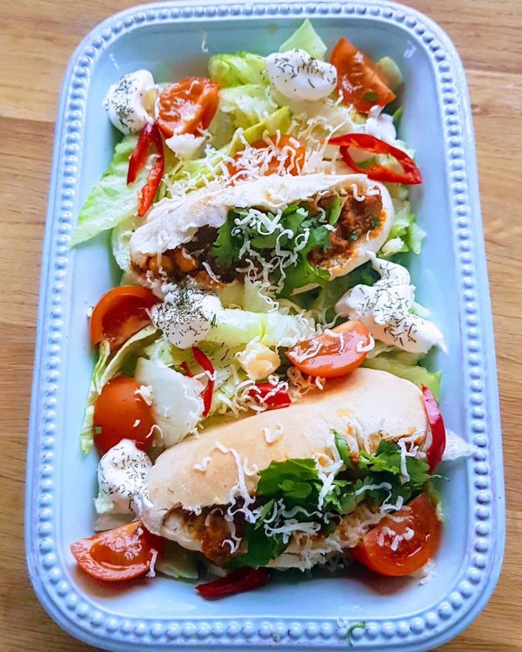Mini pittas stuffed with plant-based chilli, served with salad, cherry tomatoes, sour cream, cheddar and fresh coriander