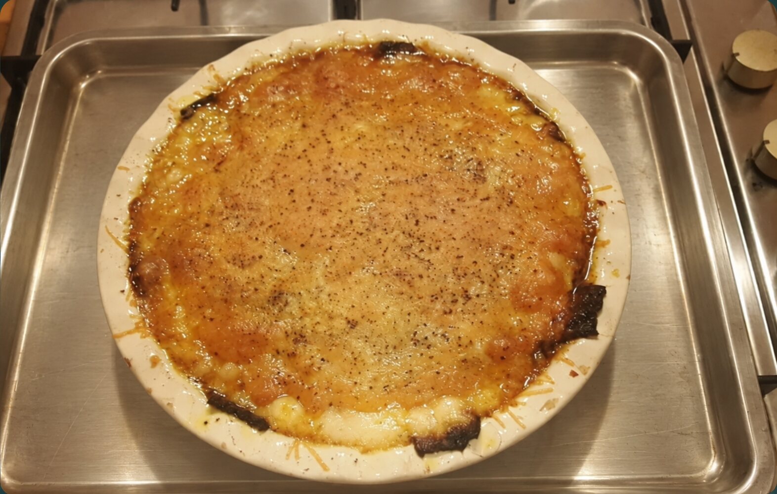 A golden courgette, beef and potato bake in a ceramic dish on a clean metal baking tray