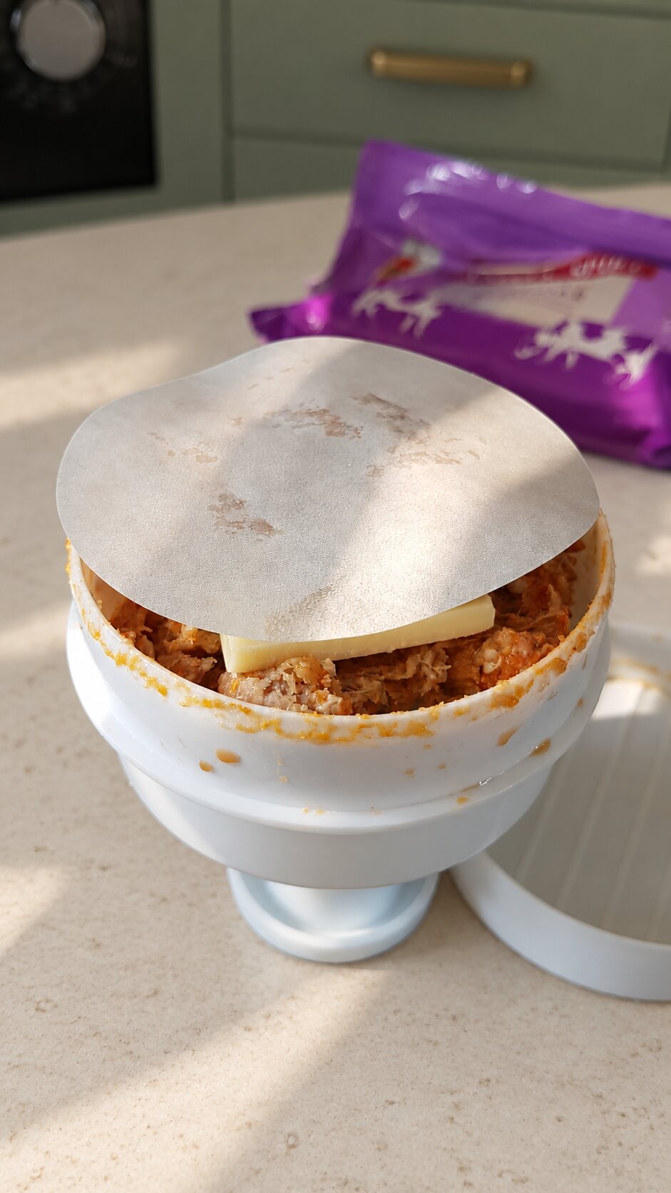 A separating paper covering a cheese-stuffed burger before pressing