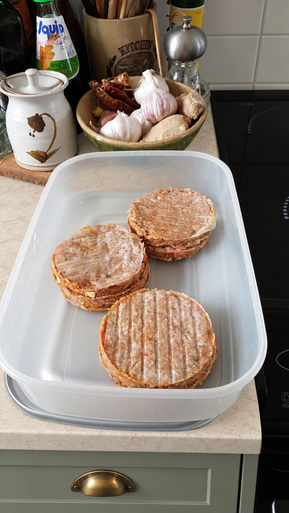Stacks of freshly formed homemade burgers in a container on a pale stone kitchen worktop